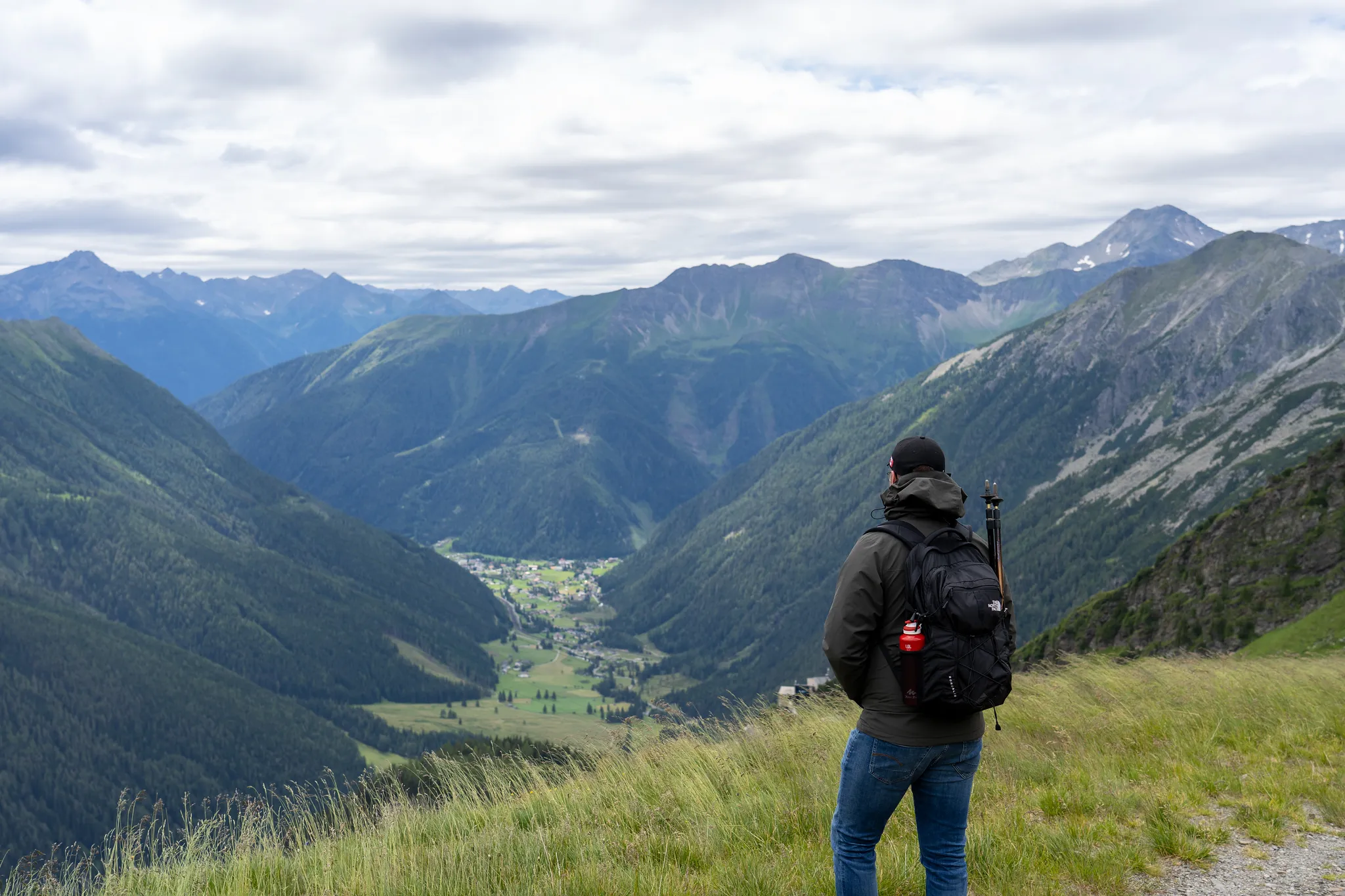 Hiker overlooking a green alpine valley and village from a mountain trail in Austria